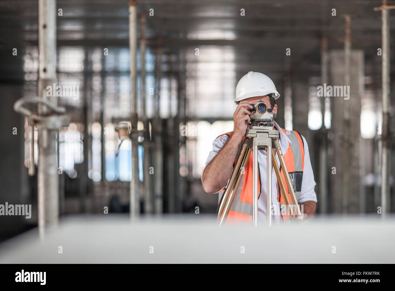 Mid adult male surveyor looking through theodolite on construction site Stock Photo
