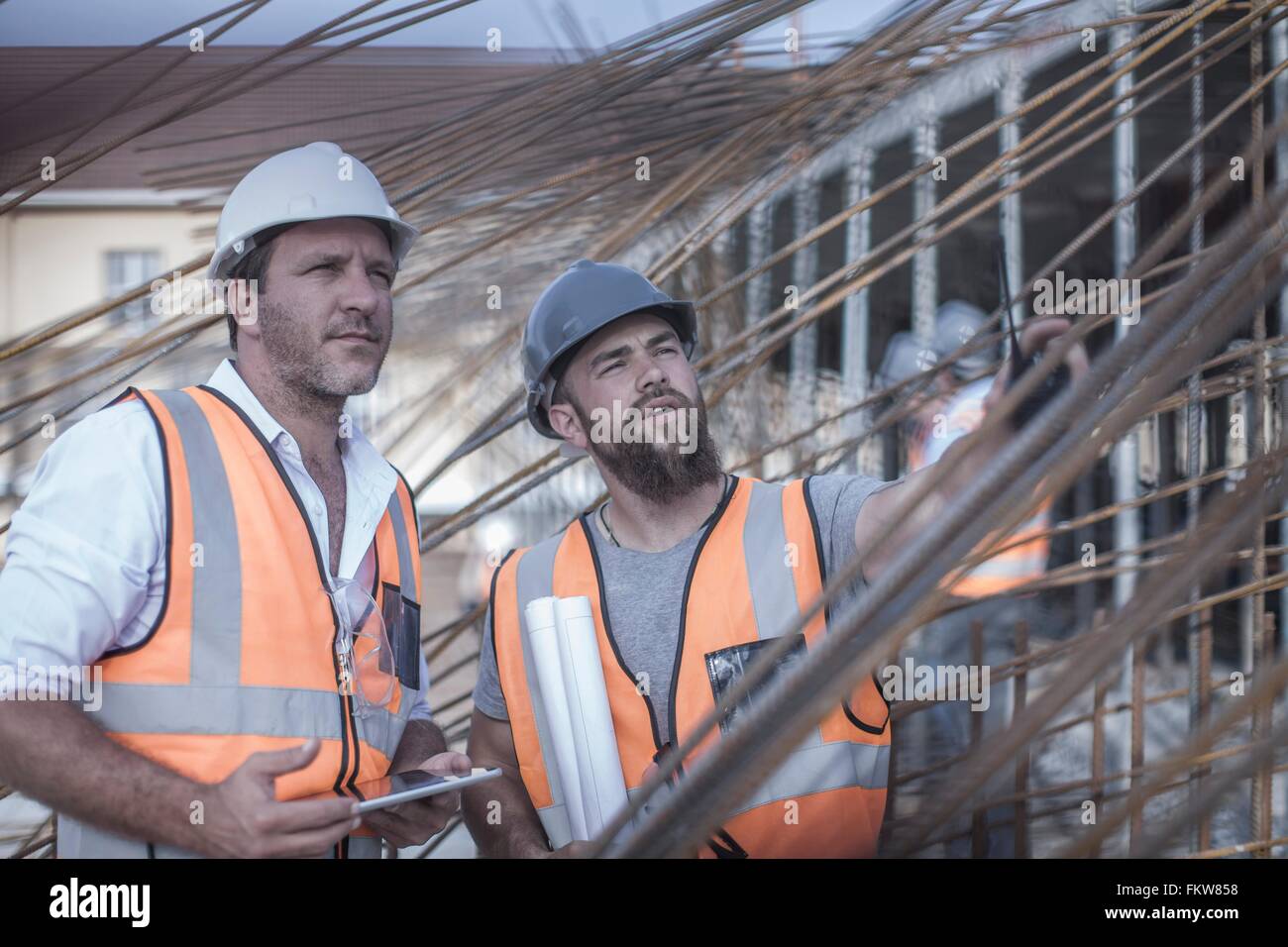 Site manager and builder discussing steel rod structures on