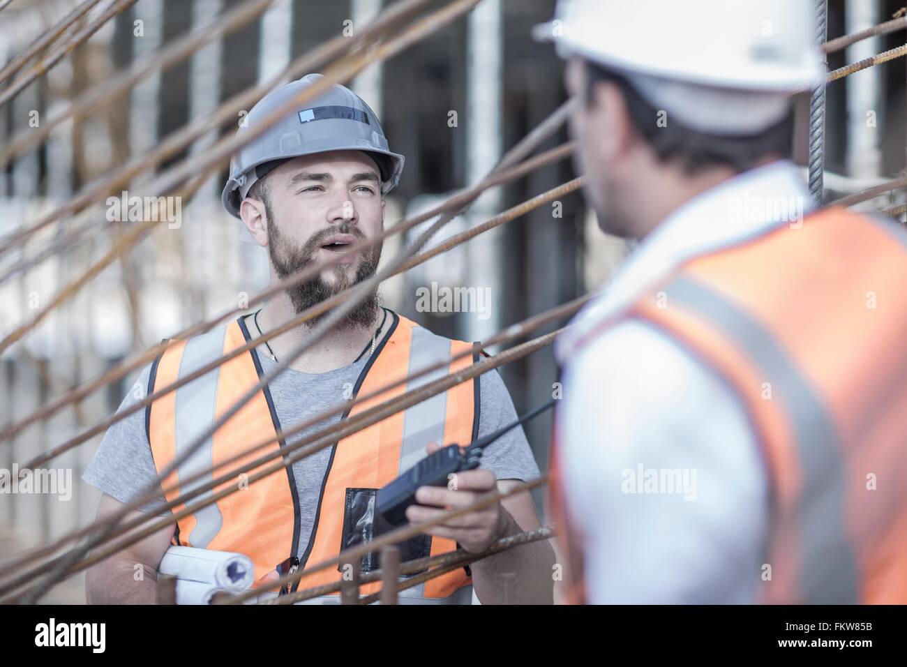 Site manager and builder discussing steel rods on construction site