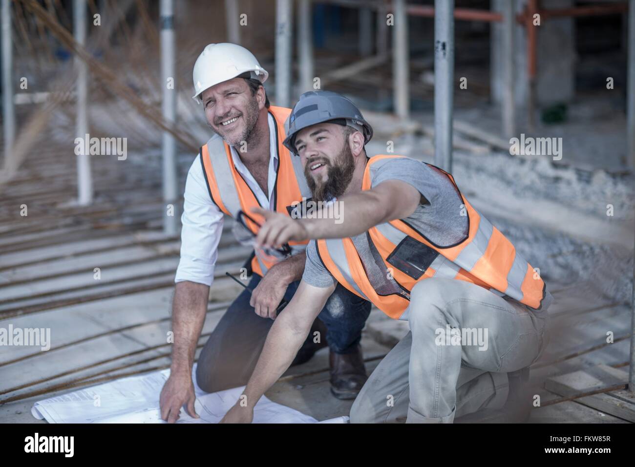 Site manager and builder with blueprint on construction site Stock Photo