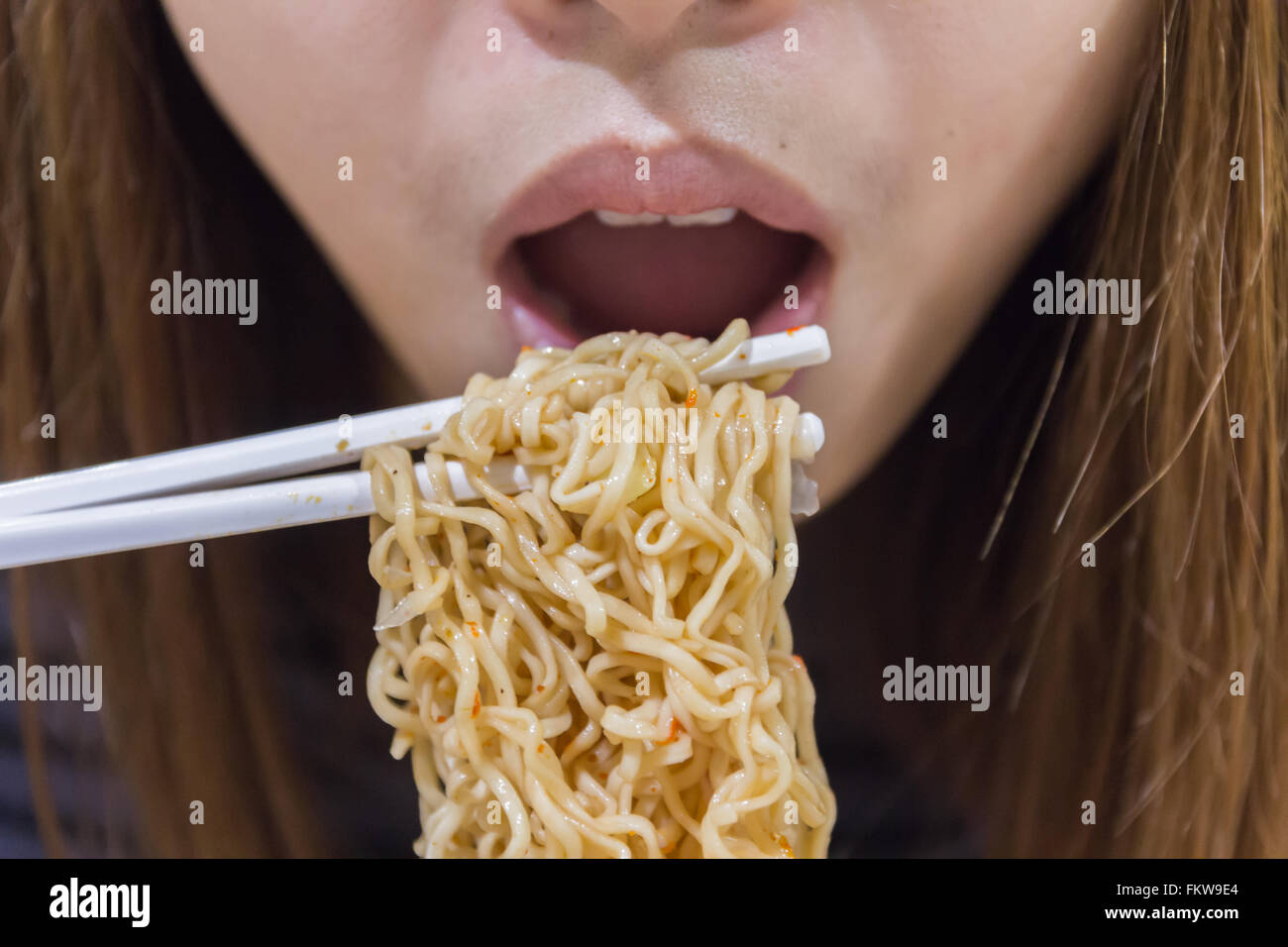 Noodle on chopsticks with people in background, shallow depth of field Stock Photo