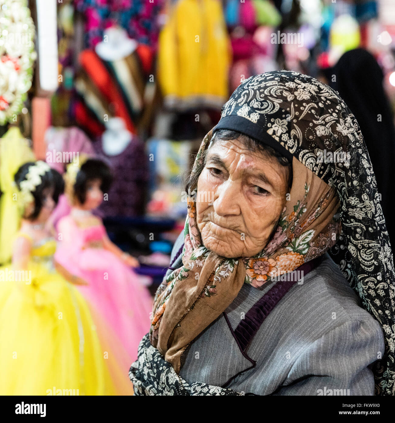 Elderly woman in hijab stands in front of a Vakil bazaar stall at which dolls are sold. Shiraz, Iran Stock Photo