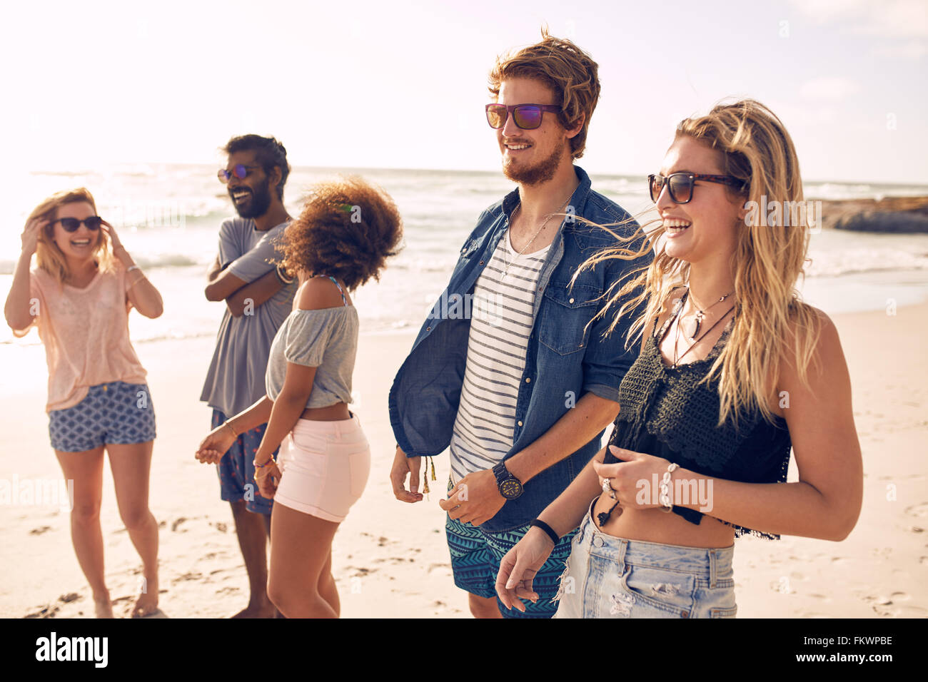 Group of friends walking along a beach at summertime. Happy young people enjoying a day at beach. Stock Photo