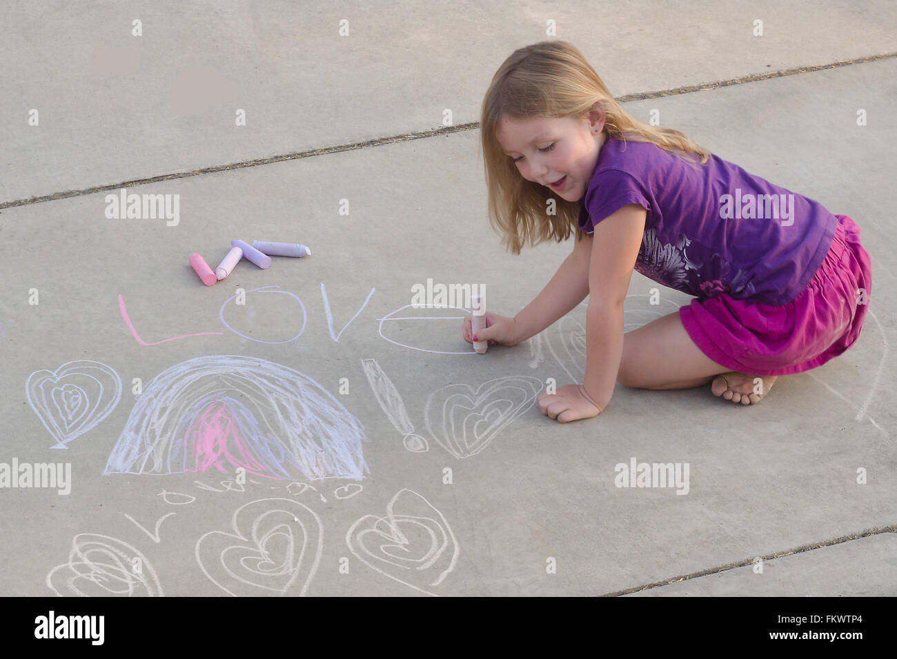 A six year old girl creates her designs on a sidewalk with chalk Stock Photo