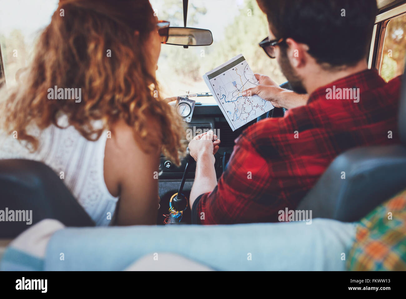 Rear view of a young couple in their car checking a map. Young man and woman on a road trip. Stock Photo