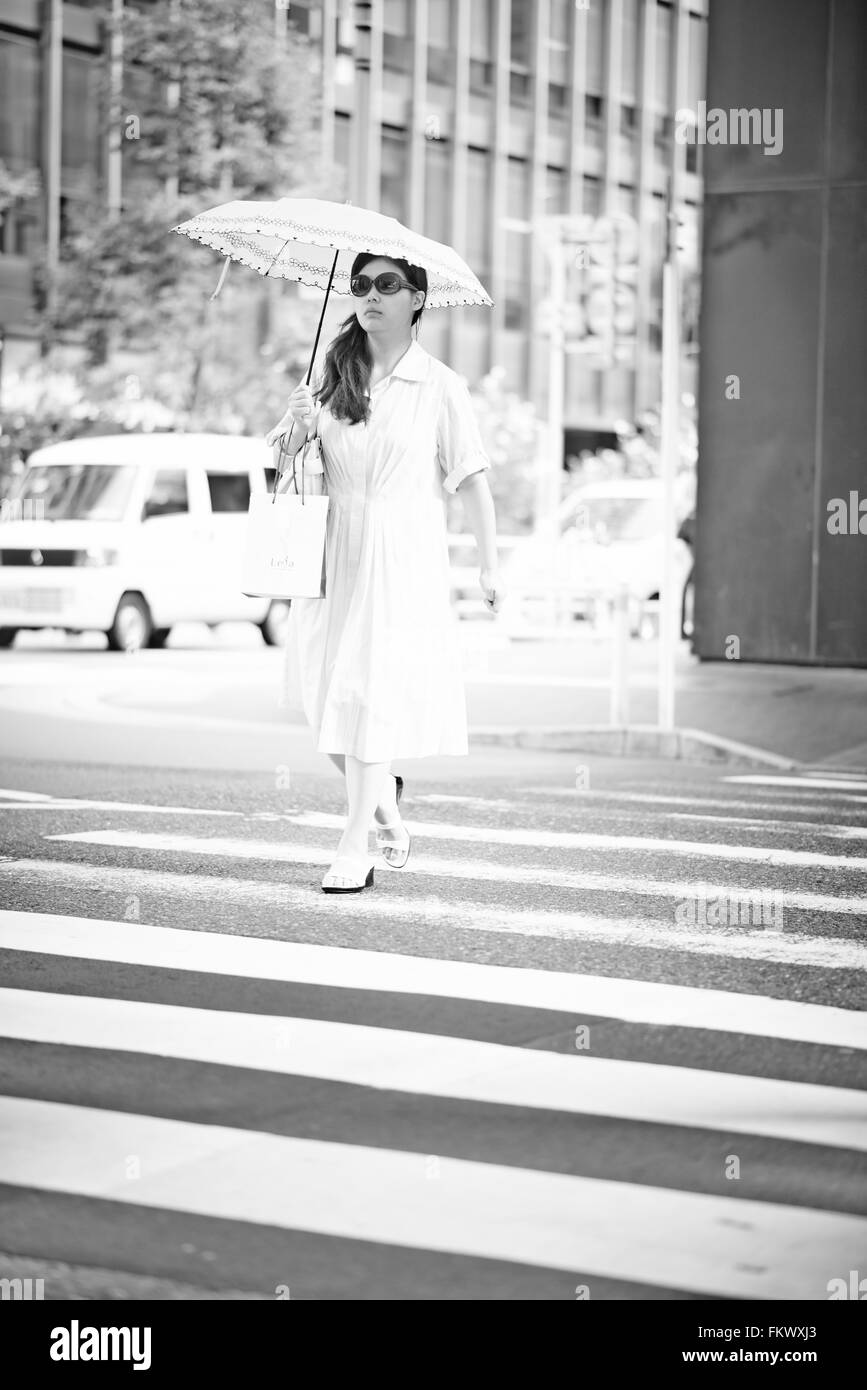 Japanese woman all in white with umbrella crossing street Stock Photo