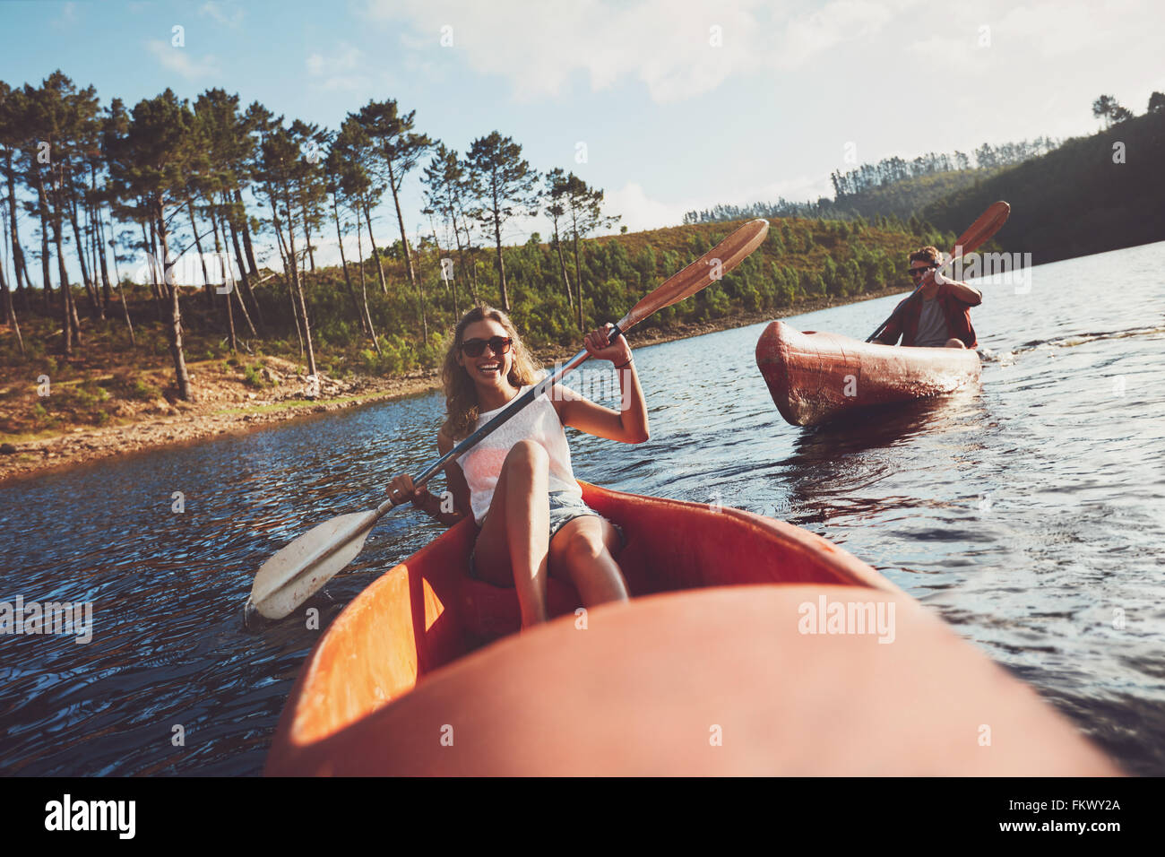 Young people kayaking on a lake. Smiling young woman kayakers with a man paddling kayak in the background. Stock Photo