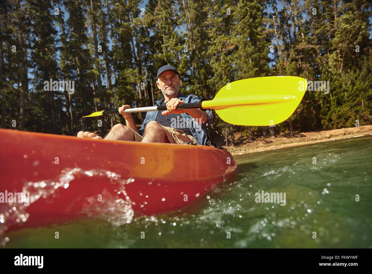 Senior caucasian man paddling a kayak in lake. Mature man canoeing on summer day. Stock Photo