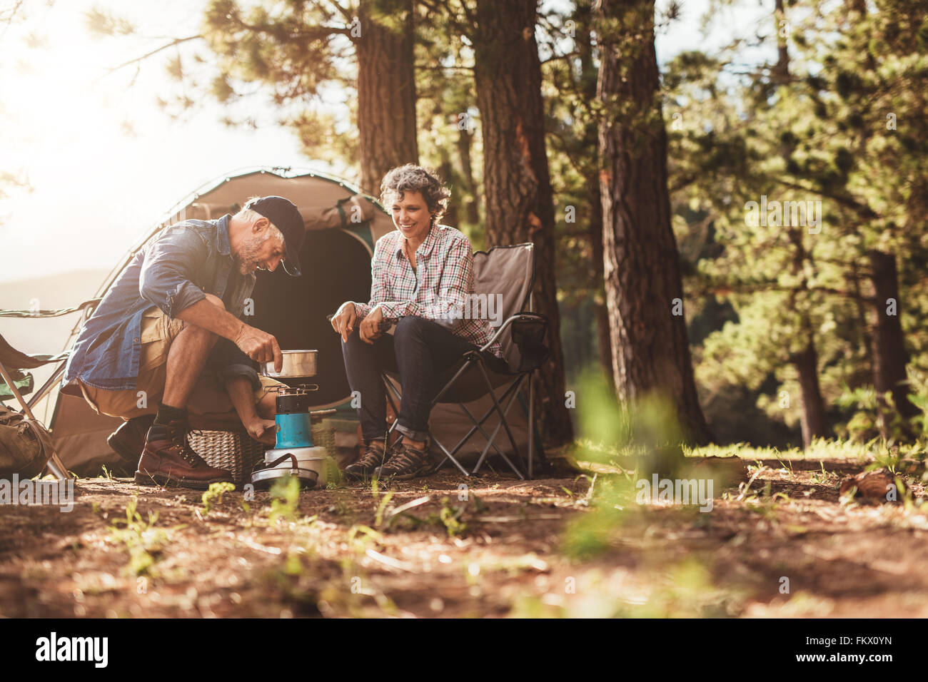 Happy campers outdoors in the wilderness and making coffee on a stove. Senior couple on a camping holiday. Stock Photo