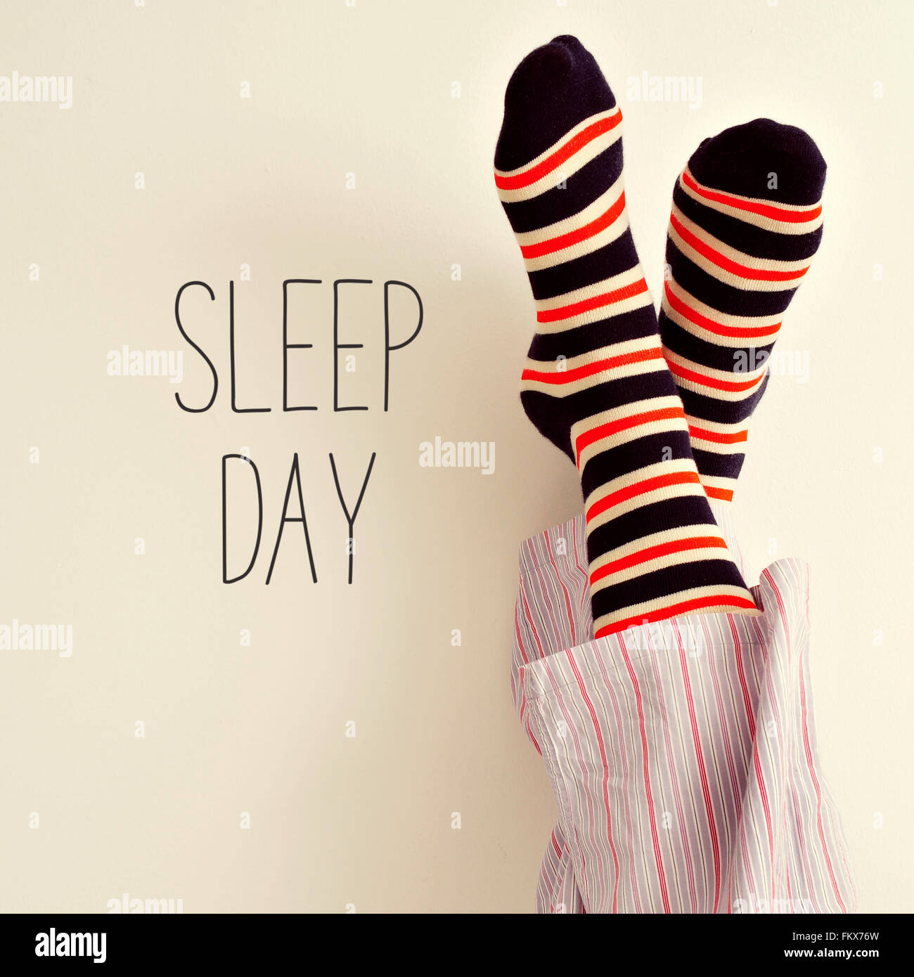 closeup of a young man in pajamas wearing colorful striped socks with his feet against the wall and the text sleep day Stock Photo