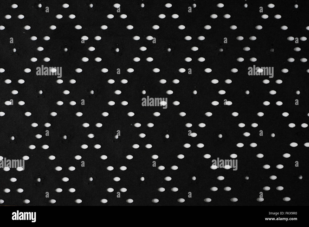 Black perforated striped paper sheet texture background. Ovals, squares, flowers shapes embossed pattern. Stock Photo