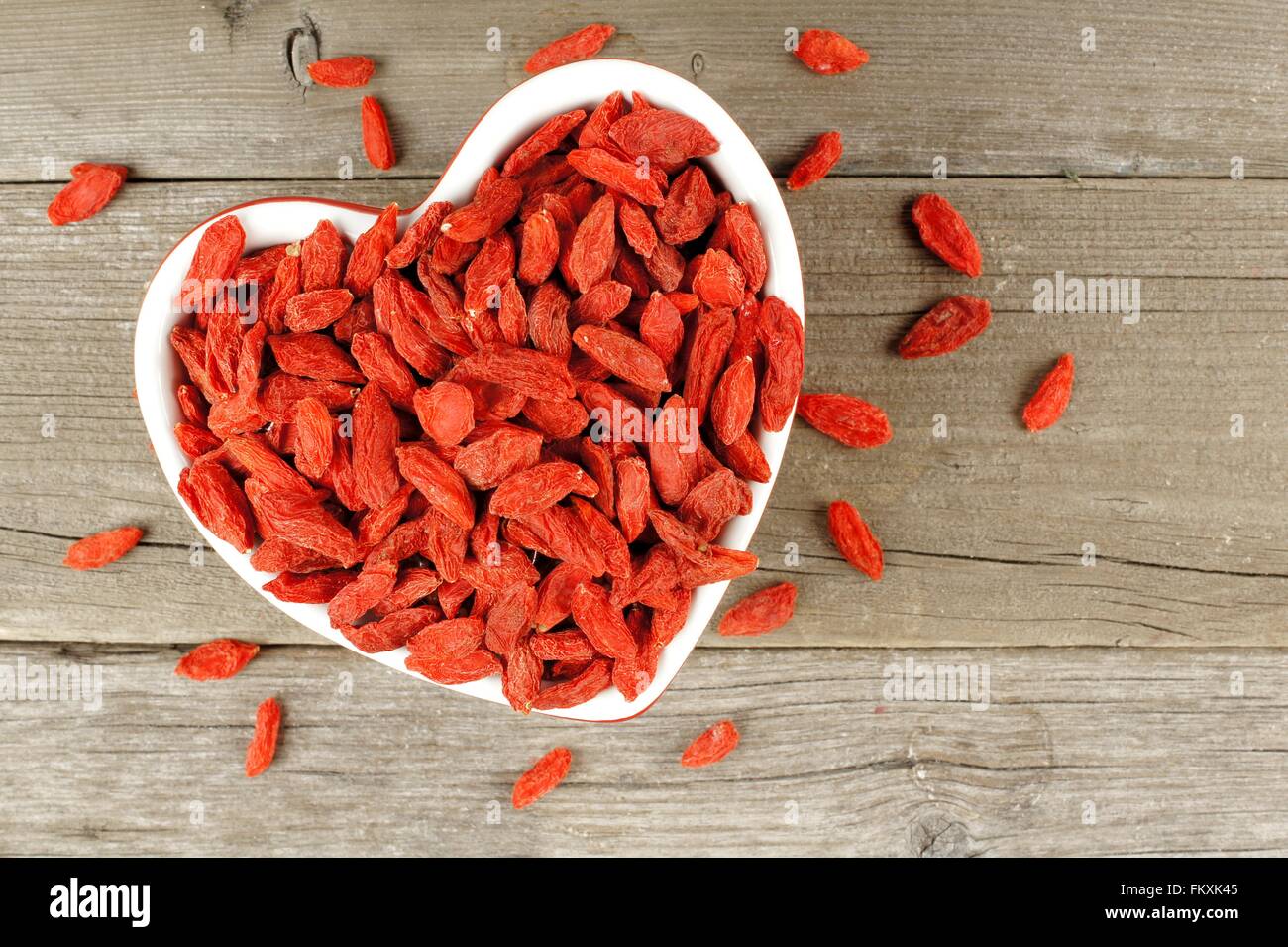 Heart shaped bowl filled with dried goji berries over a wood background Stock Photo