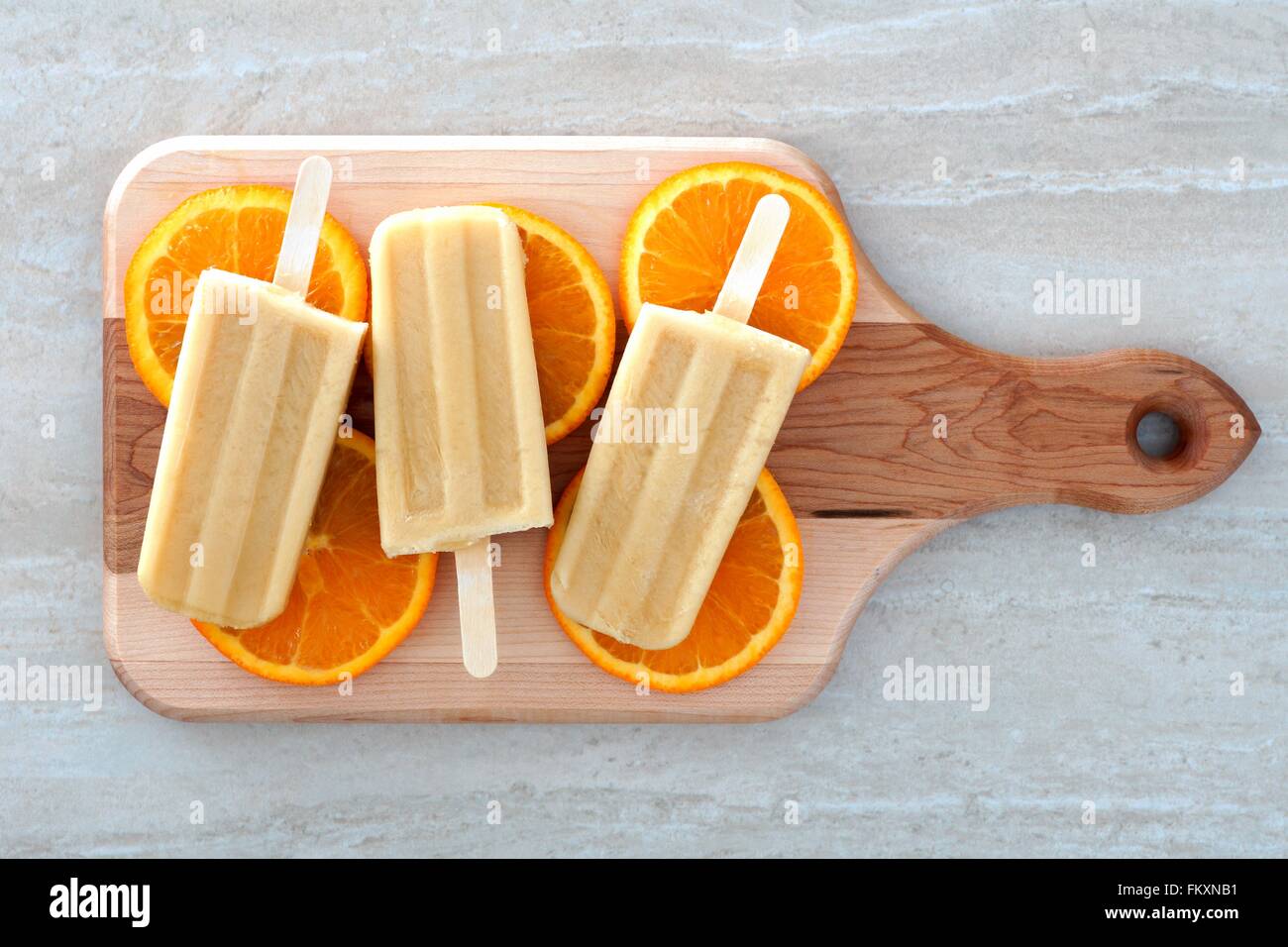 Frozen orange flavored yogurt pops with fruit slices on a wooden paddle board Stock Photo