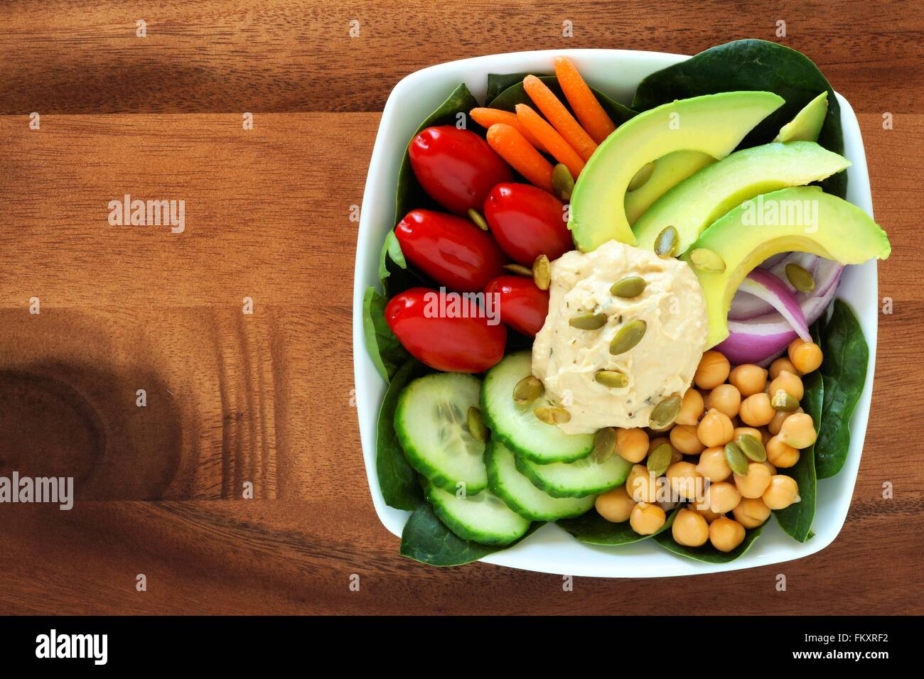Nutritious lunch bowl with avocado, hummus and mixed vegetables, overhead view in square bowl on wood Stock Photo