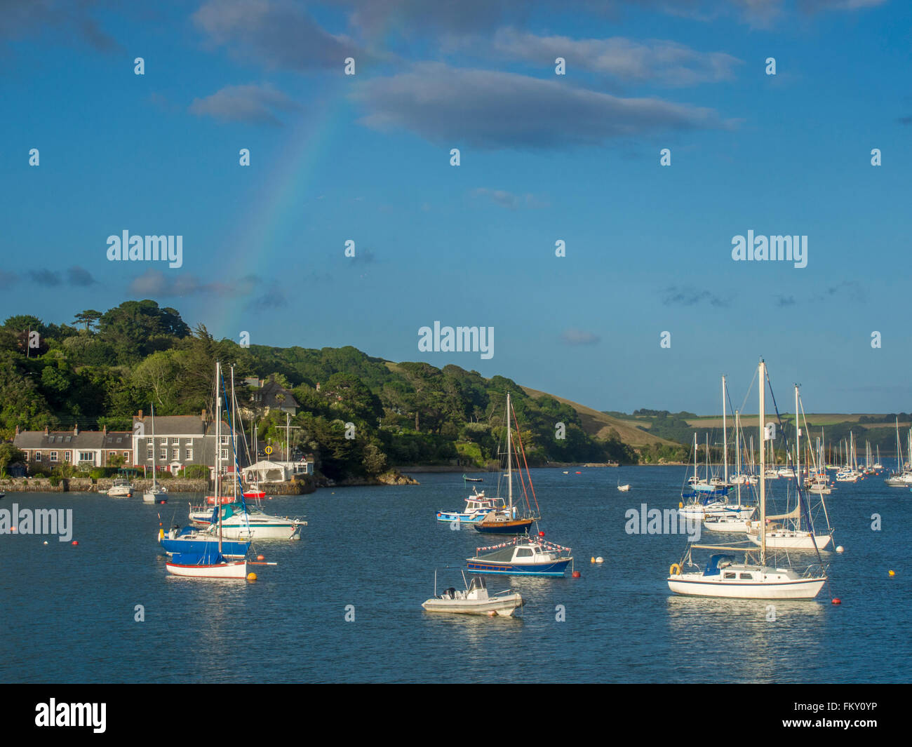 A tranquil harbour scene at Falmouth, England, showing village of Flushing and sailing boats. A faint rainbow in the sky. Stock Photo