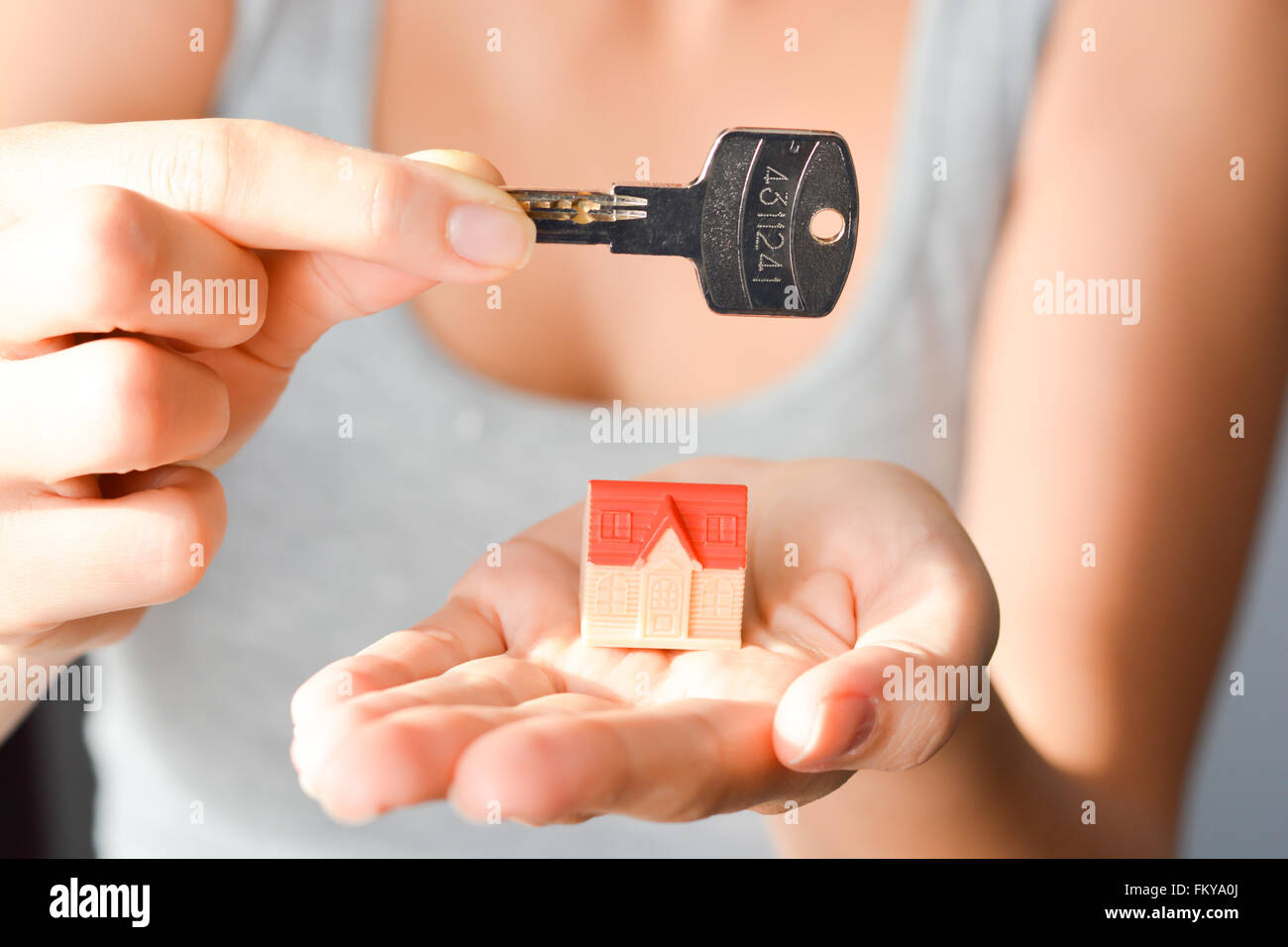 Close-up of woman's hands holding a small model house and a key suggesting house acquisition or rental Stock Photo