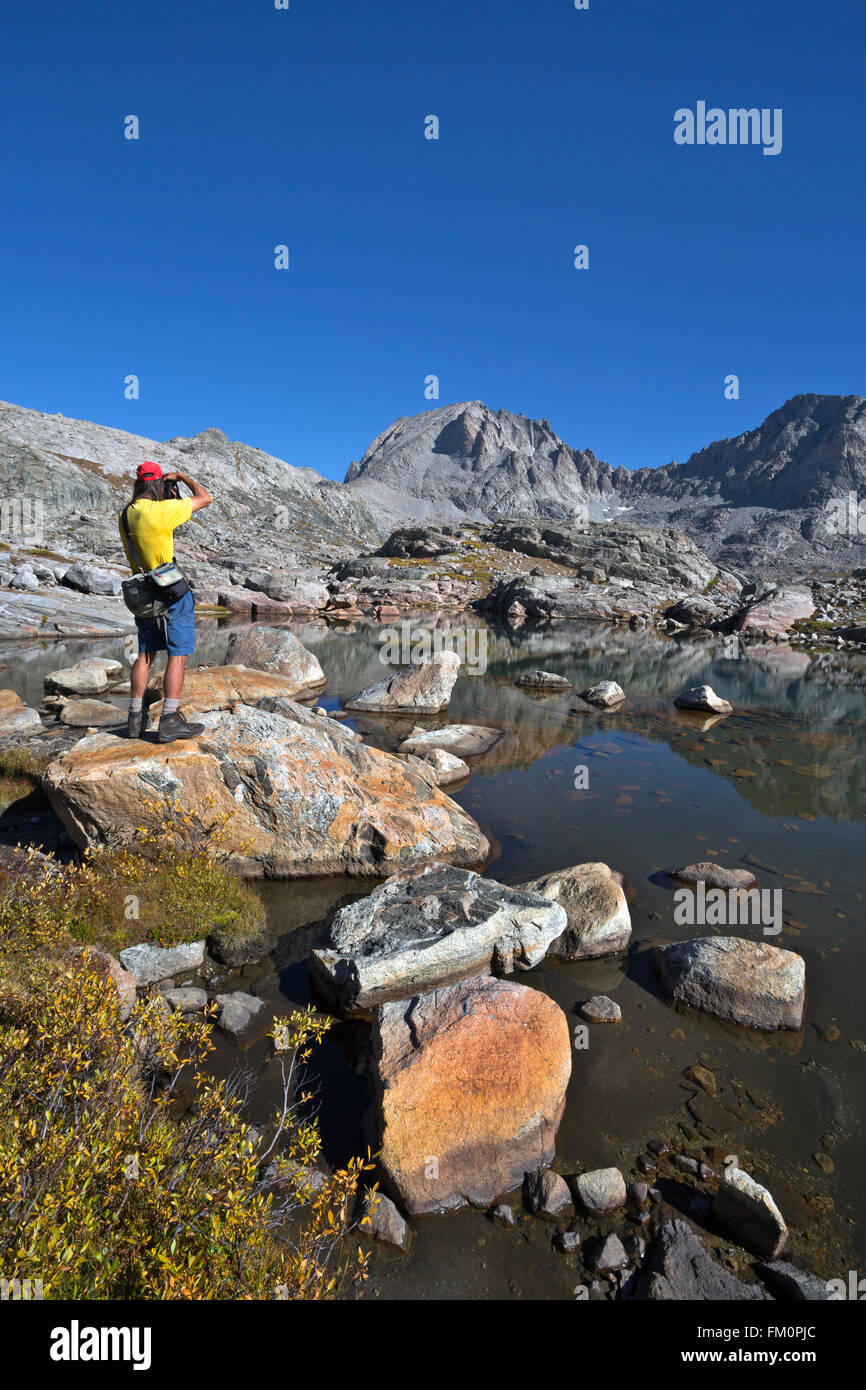 WYOMING Hiker photographing a reflection of Fremont Peak in a small lake in the Indian Basin