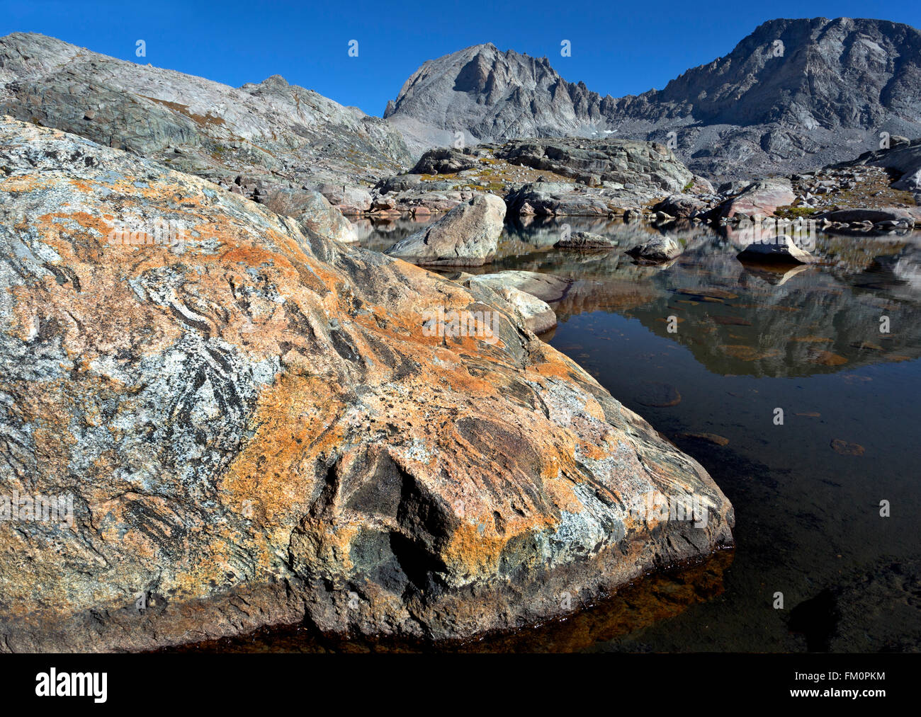 WYOMING - Colorful rock on the shore of small lake and a reflection of Fremont Peak in Indian Basin area of the Wind River Range Stock Photo