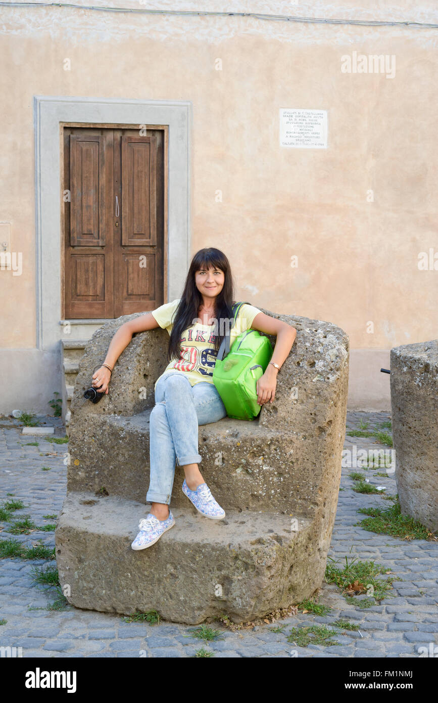 nice girl posing sitting on a rock big chair in an ancient village called Calcata, Italy Stock Photo