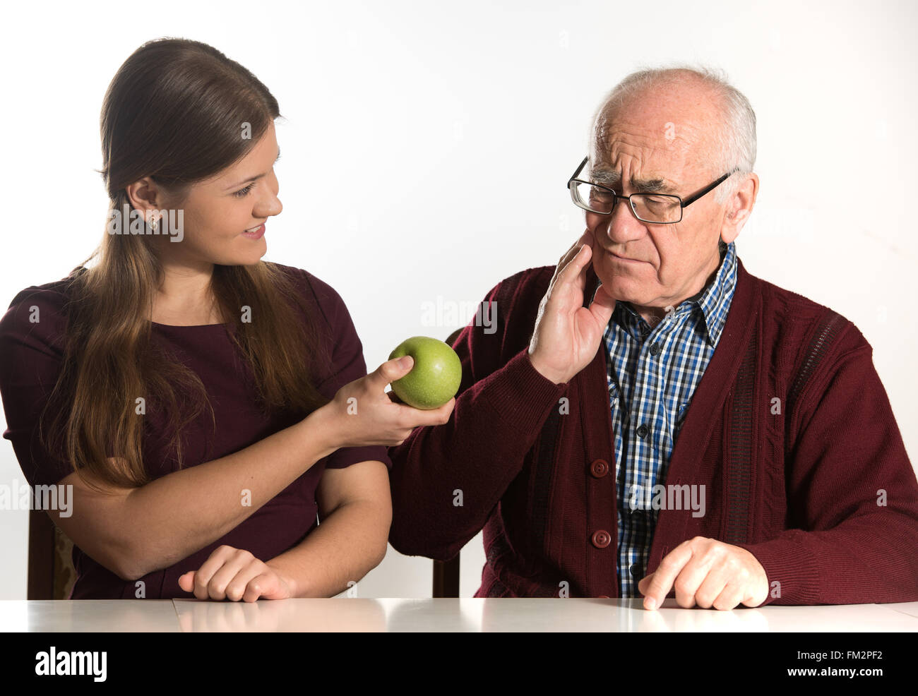young woman helps senior man to eat green apple Stock Photo