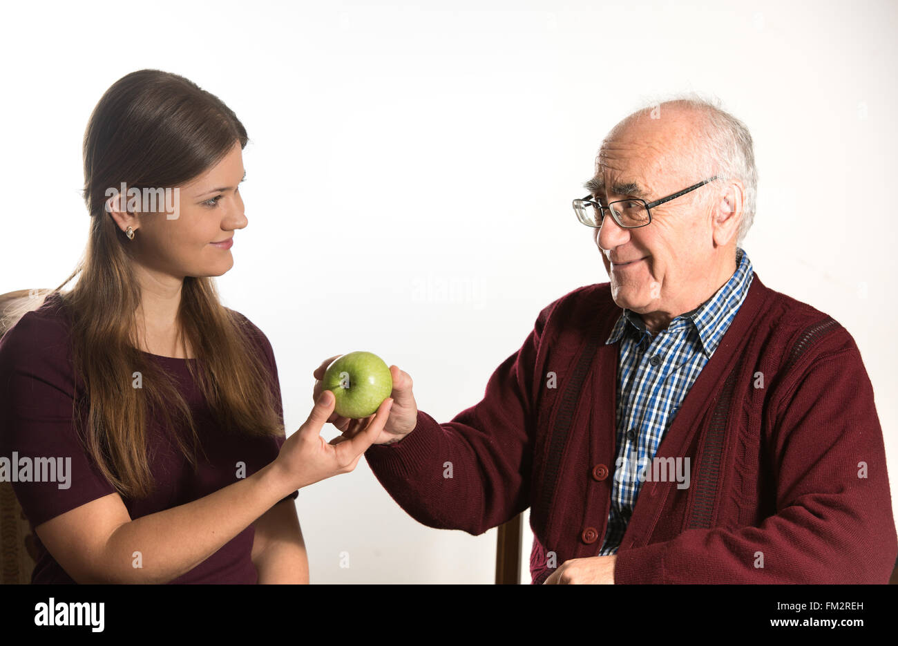 young woman helps senior man to eat green apple Stock Photo