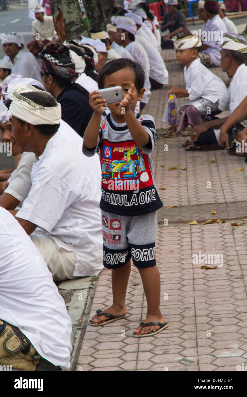 Asia, Indonesia, Bali. Child taking cell phone picture while watching a parade. Stock Photo