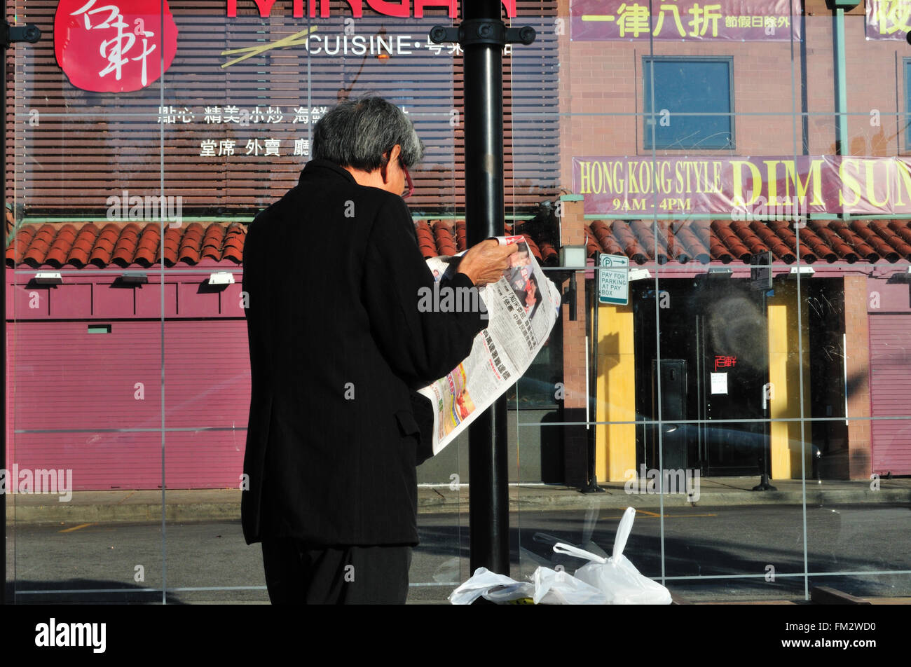 A resident of Chicago's Chinatown reads the local press while waiting for an early morning bus in his community. Chicago, Illinois, USA. Stock Photo