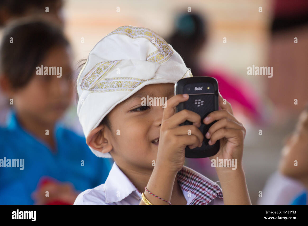 Asia, Indonesia, Bali, Pejeng. Young boy taking a picture with a mobile phone at the Hindu Temple Festival in Pejang. Stock Photo