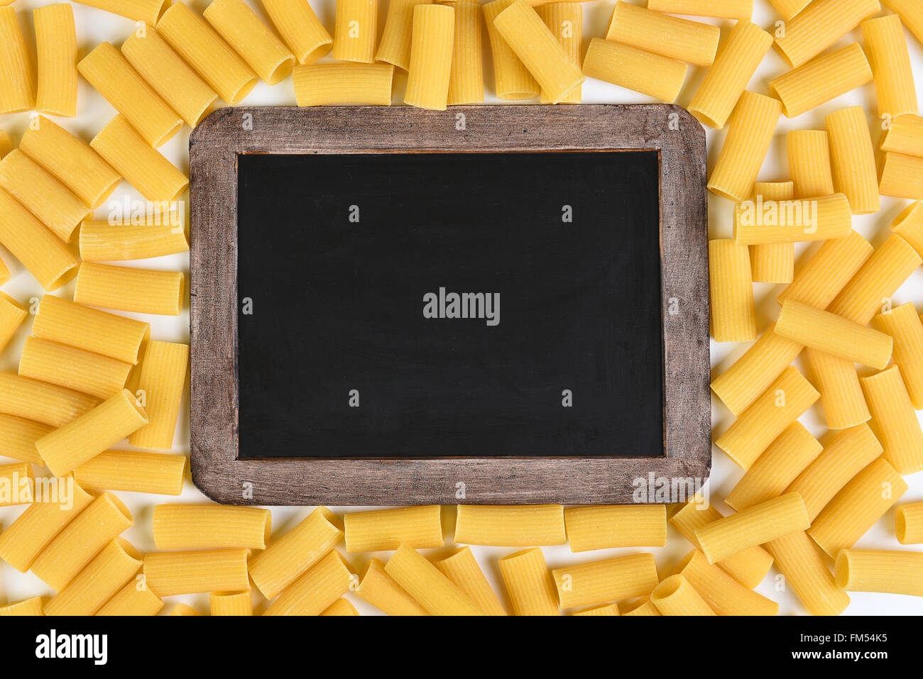 Chalkboard surrounded by rigatoni pasta. Top vies filling the frame. Stock Photo