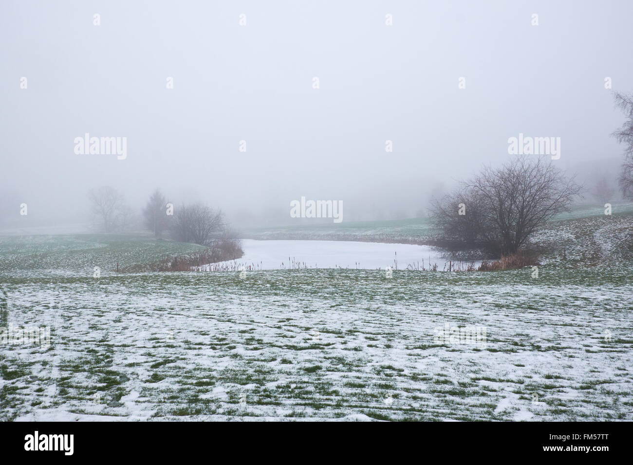 ice covered pond in snow covered meadow fields on a hazy winter day Stock Photo