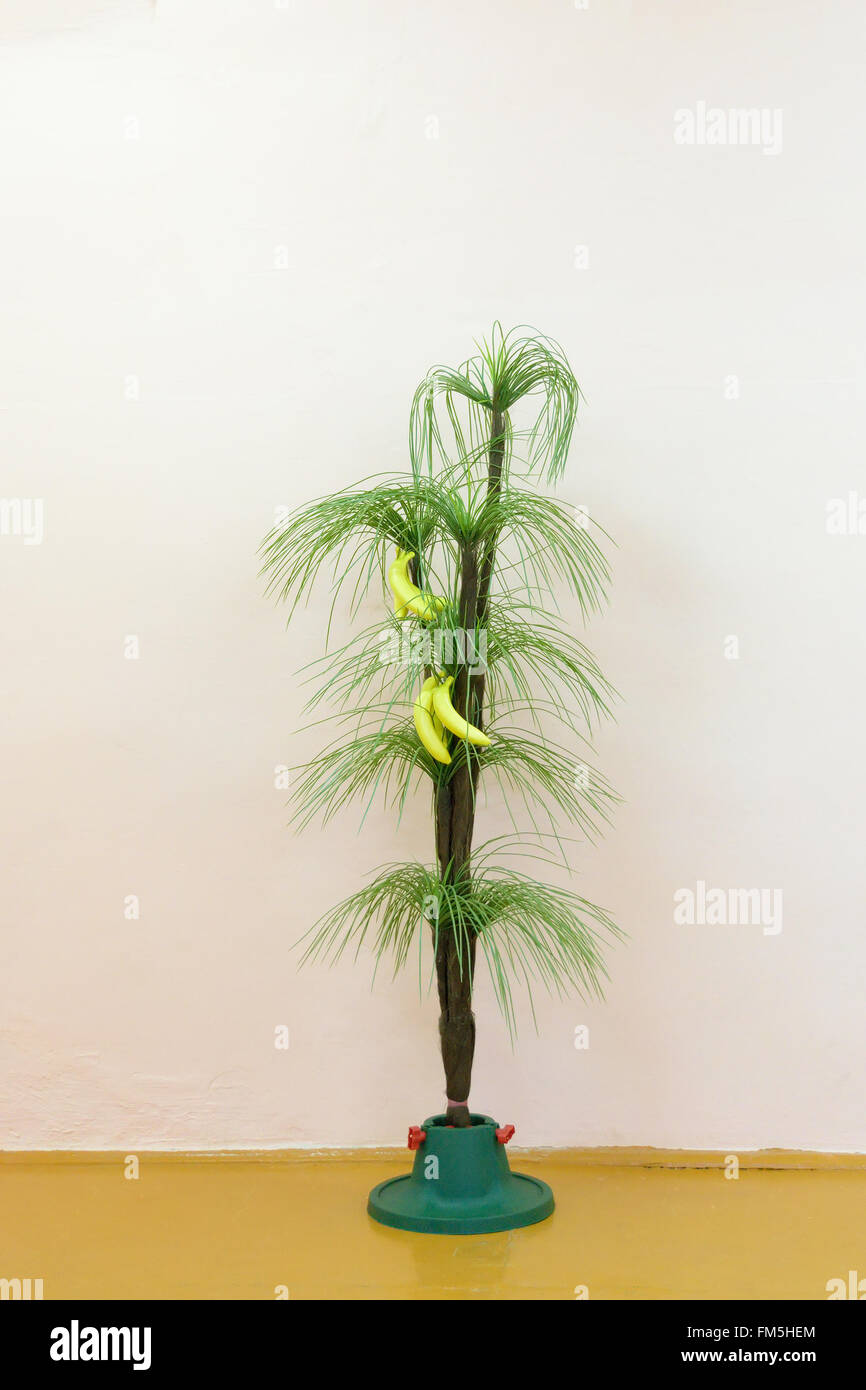 Artificial green palm with yellow bananas is on stand on the background light walls Stock Photo