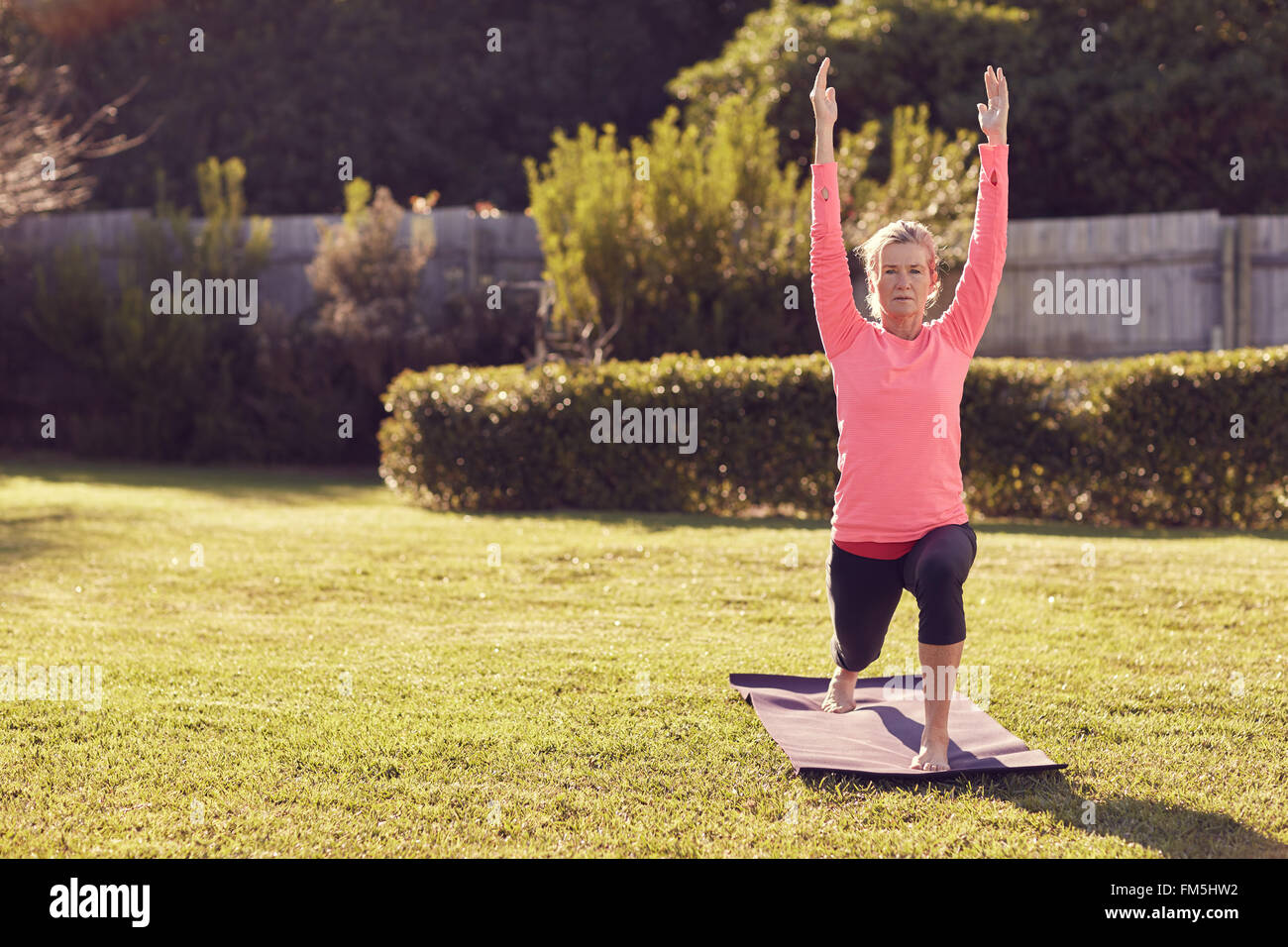 Fit senior woman doing yoga outdoors on some grass on a summer morning ...