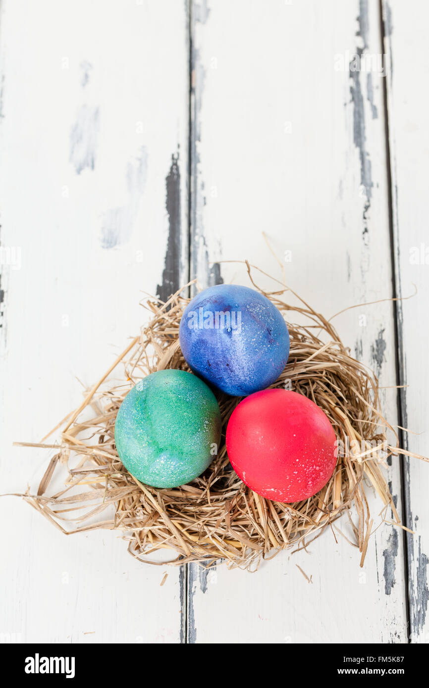 three colored eggs in a bird nest on white wooden vintage background ...