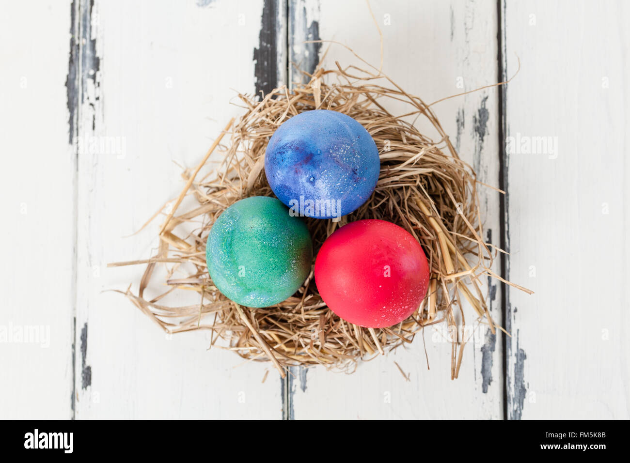 three colored eggs in a bird nest from above Stock Photo