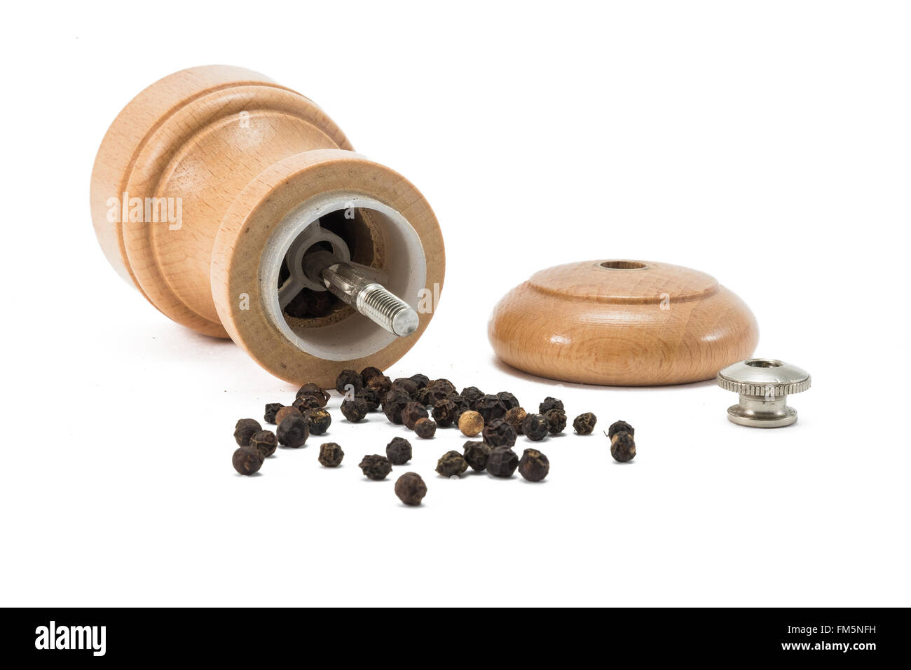 Small pepper grinder of wood lying with the lid of and with pepper corns spread around on white background Stock Photo