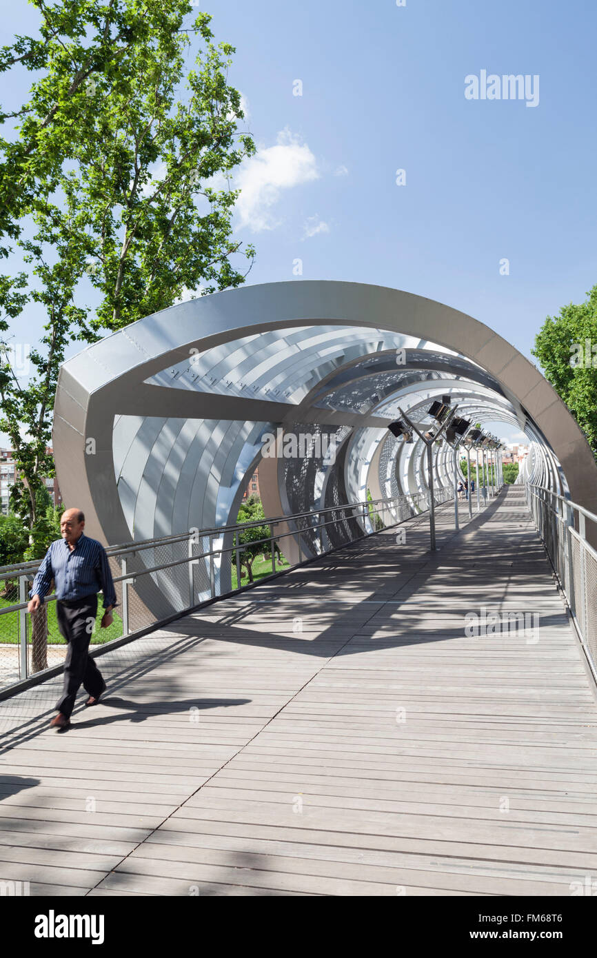 A view of a modern new metal structure in Madrid called The Pasarela del Arganzuela as a male pedestrian crosses this unusual bridge. Stock Photo