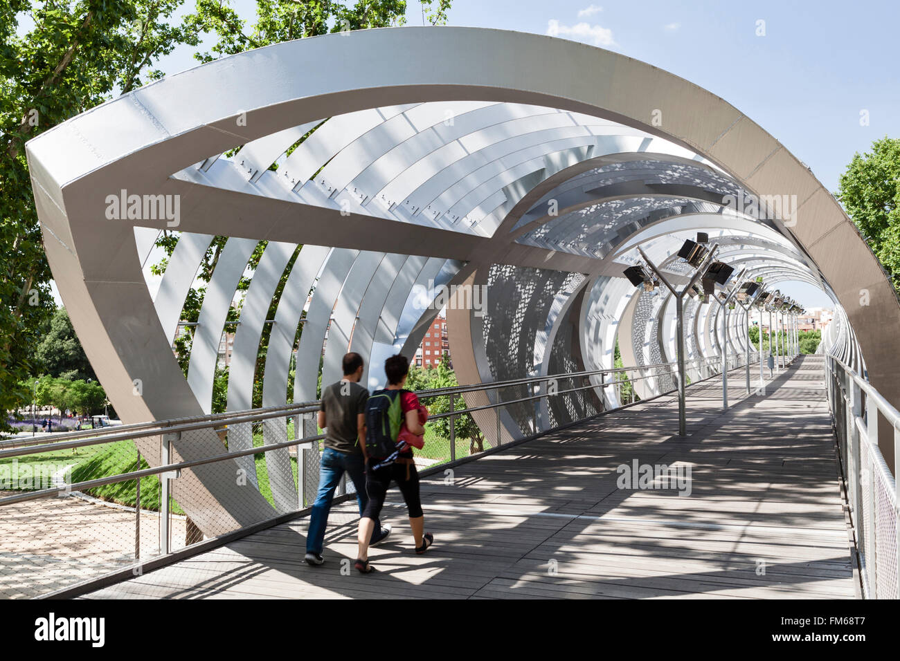 A view of a modern new metal structure in Madrid called The Pasarela del Arganzuela as a male pedestrian couple crosses this unusual bridge. Stock Photo