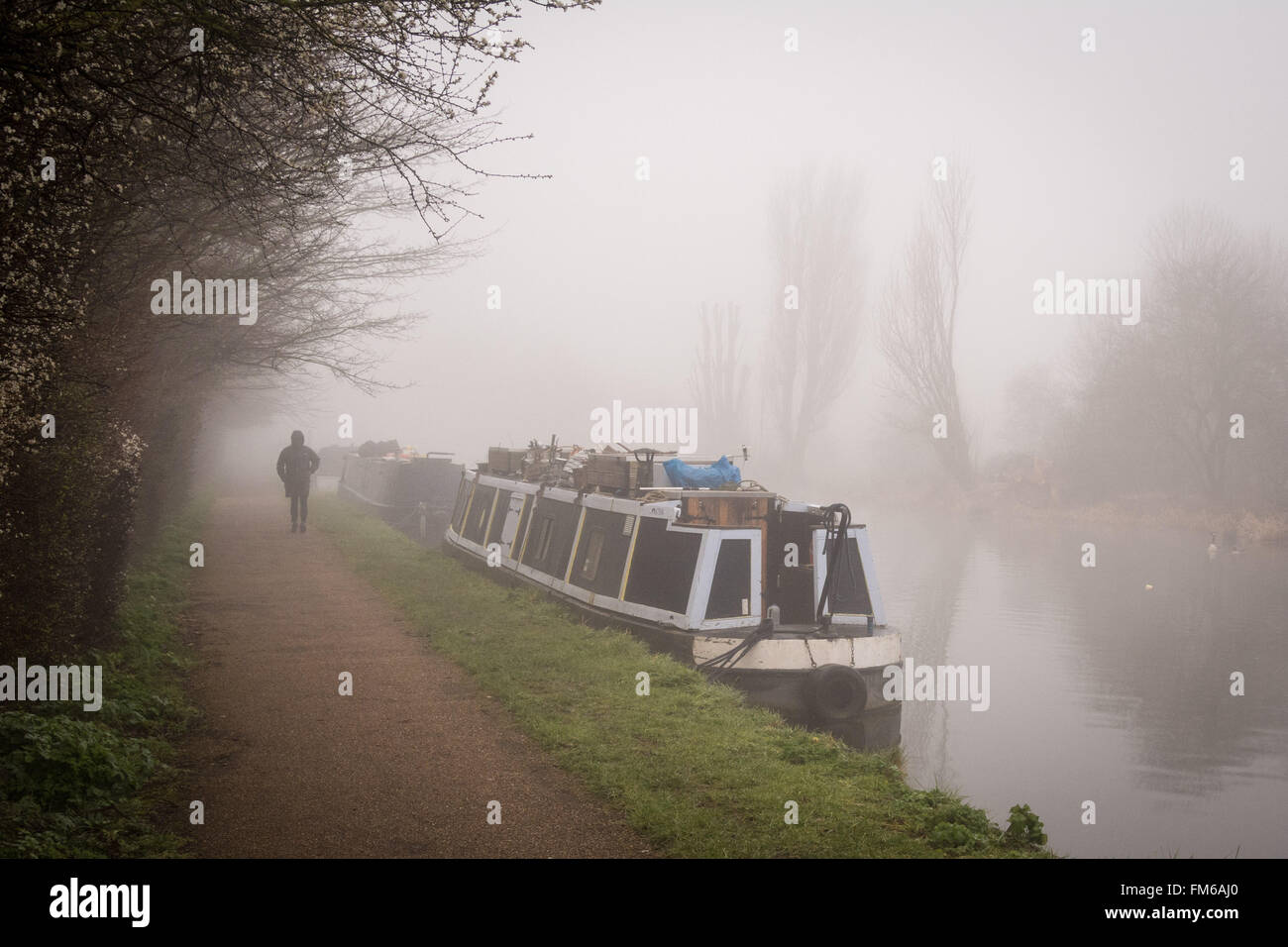A man walks along the towpath beside some houseboats on a morning of dense fog on the River Lee navigation, Tottenham, London. Credit: Patricia Phillips/Alamy Live News Stock Photo