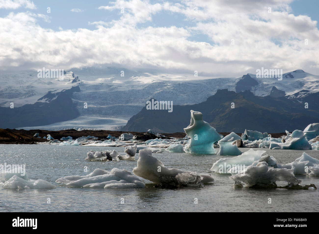 A stunning landscape of a lagoon in Iceland, with the ice cold water and small icebergs, and snowy mountains in the background. Stock Photo