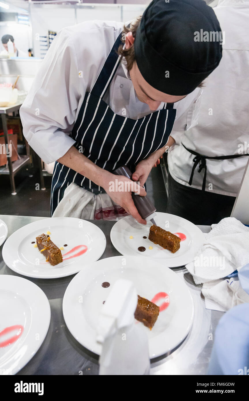 A young chef prepares desserts in a busy restaurant kitchen. Stock Photo