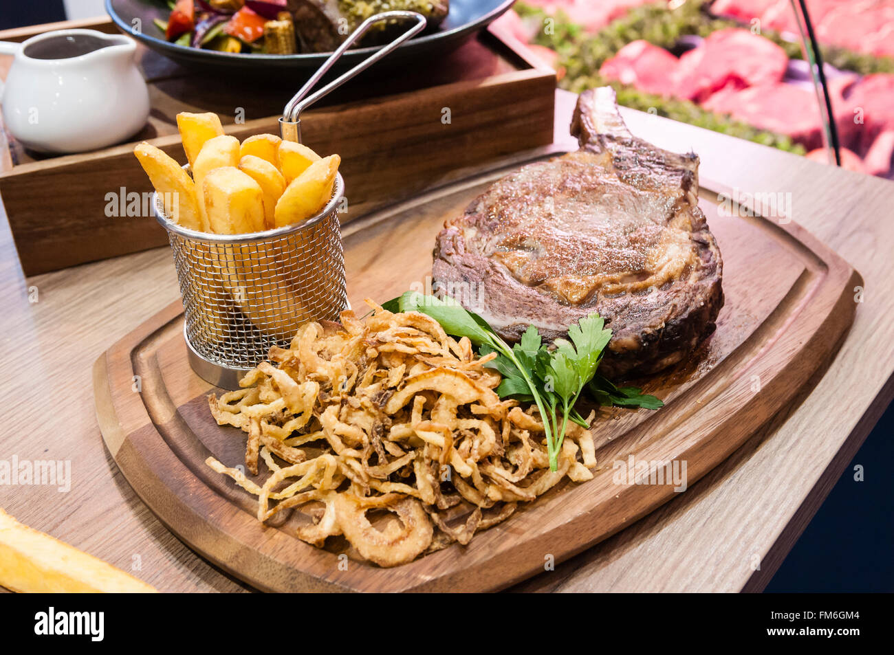 32oz tomahawk steak, chips and tobacco onions, presented on a wooden chopping board and wire basket. Stock Photo