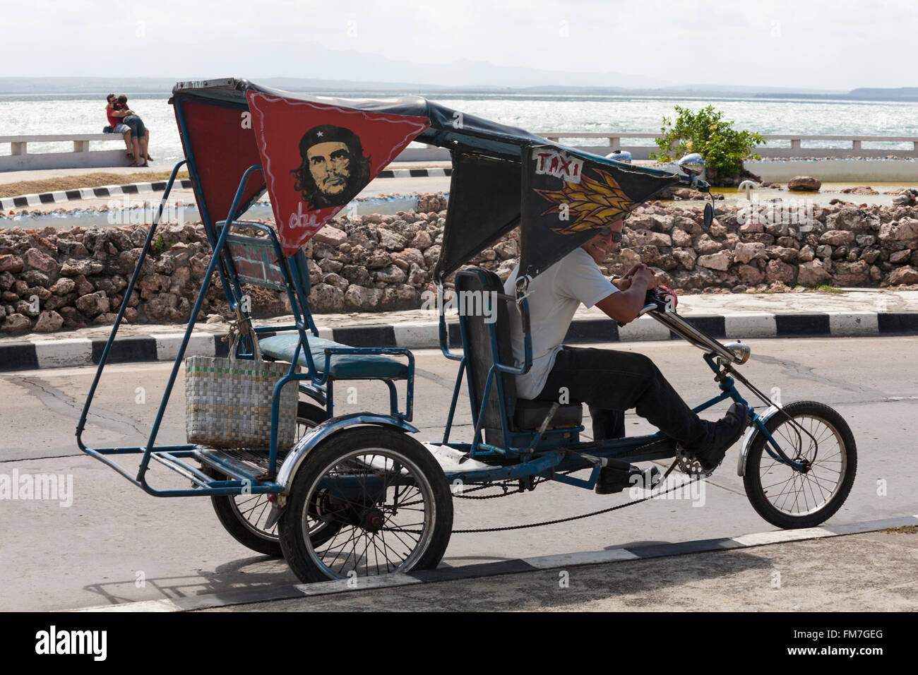 Daily life in Cuba Local man riding bicycle taxi along seafront at
