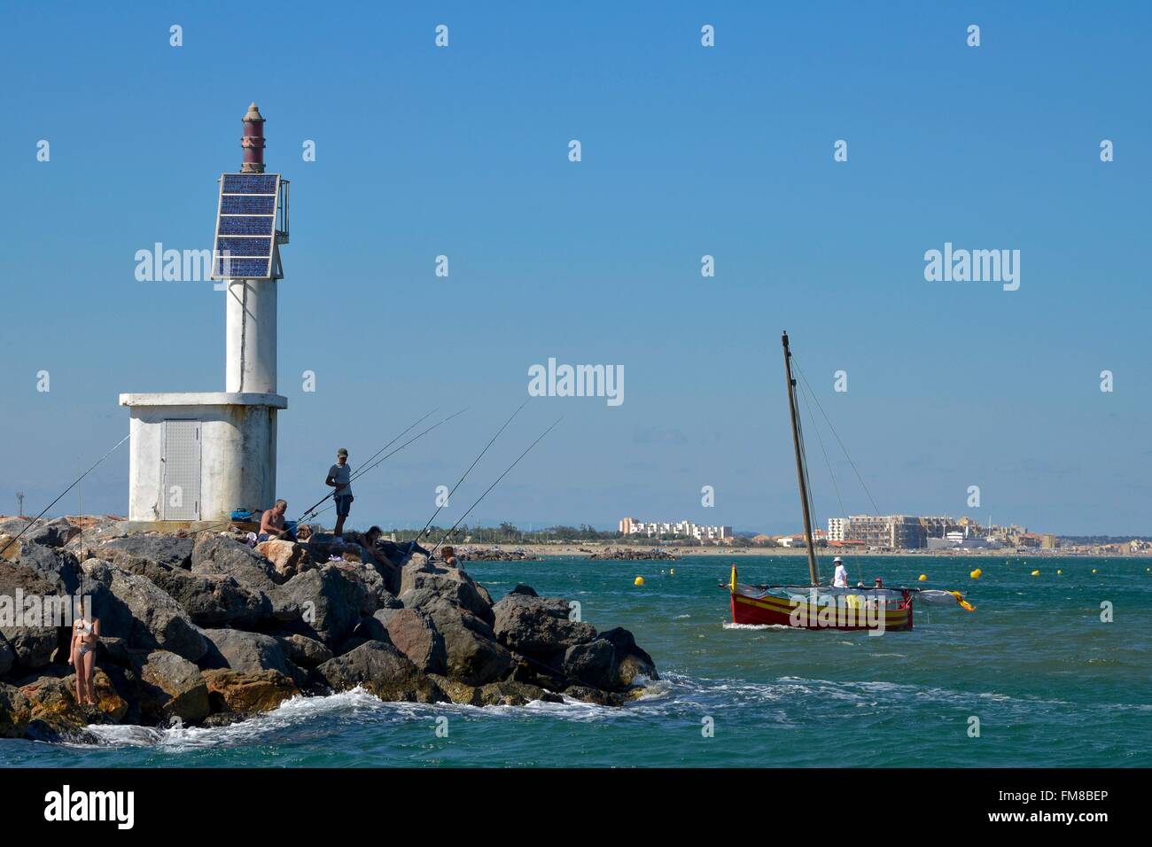 France, Aude, Port Barcares, fishermen on the rocks of the Point of Grau Saint Ange with a lateen sail in the background Stock Photo