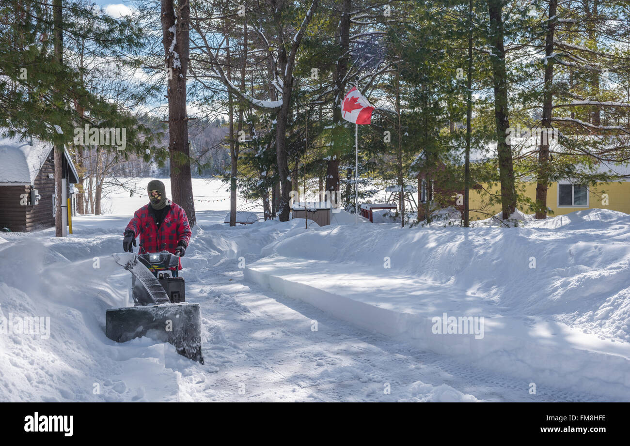 A man dress in winter work wear operating a snow thrower on a
