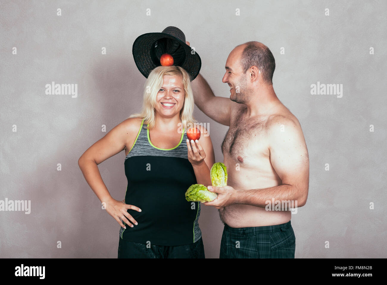 Cheerful young corpulent couple with lettuce and nectarine. Stock Photo
