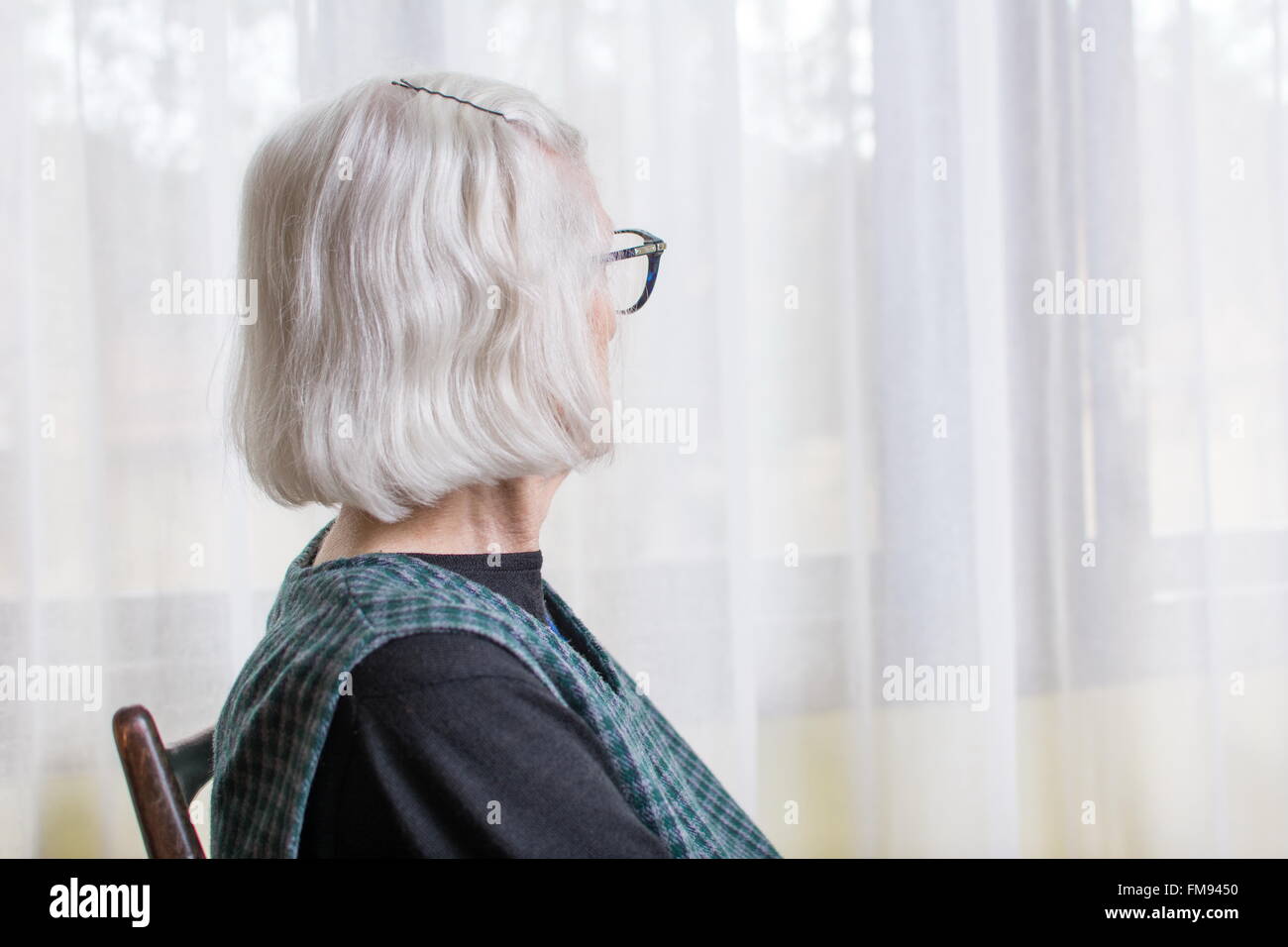 Old lady looking at her window to outdoors Stock Photo