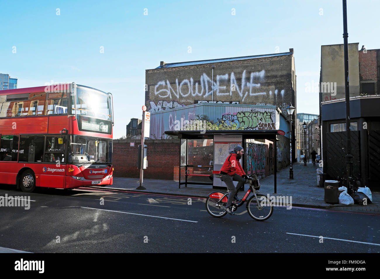 Cyclist and bus passing Edward Snowden graffiti in Shoreditch street London UK  KATHY DEWITT Stock Photo