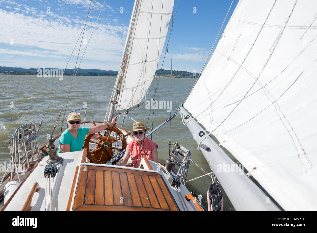 A happy senior couple enjoys time together sailing on a lake on a fine summer day. Stock Photo