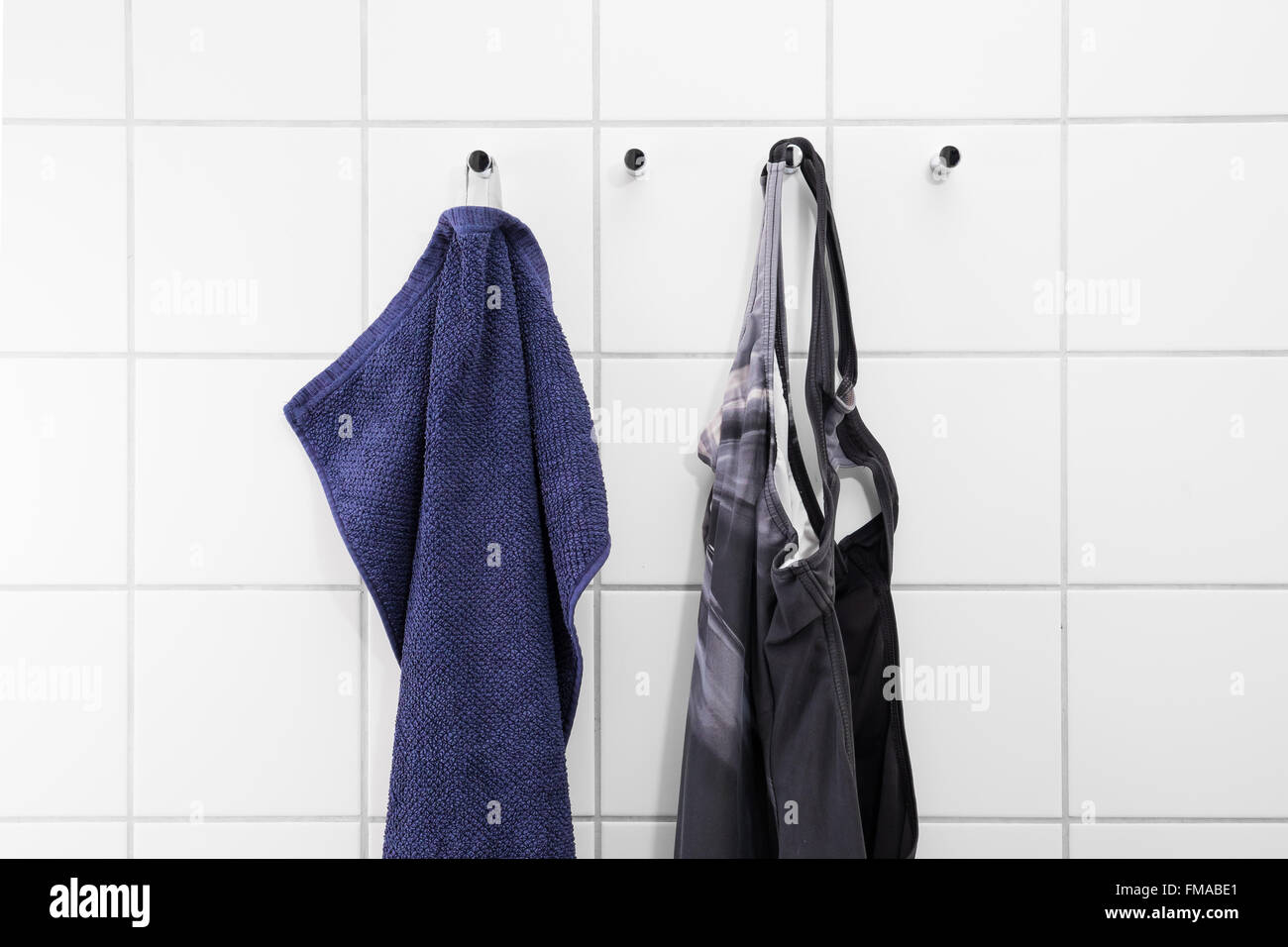 Towel and swimsuit hanging on a white tile wall of a changing room at a swimming bath Stock Photo
