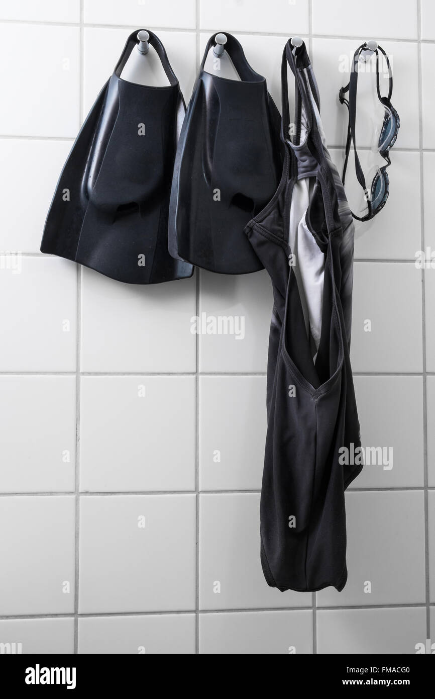 flippers, goggles and a swimsuit hanging on a white tile wall in a changing room Stock Photo